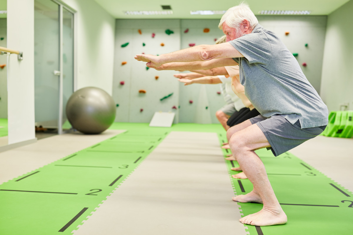 Senior group in fitness class trains strength and leg muscles with squats