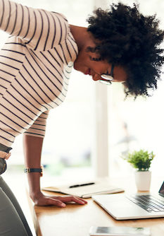 Cropped shot of a young woman holding her sore back while getting up from her desk at home